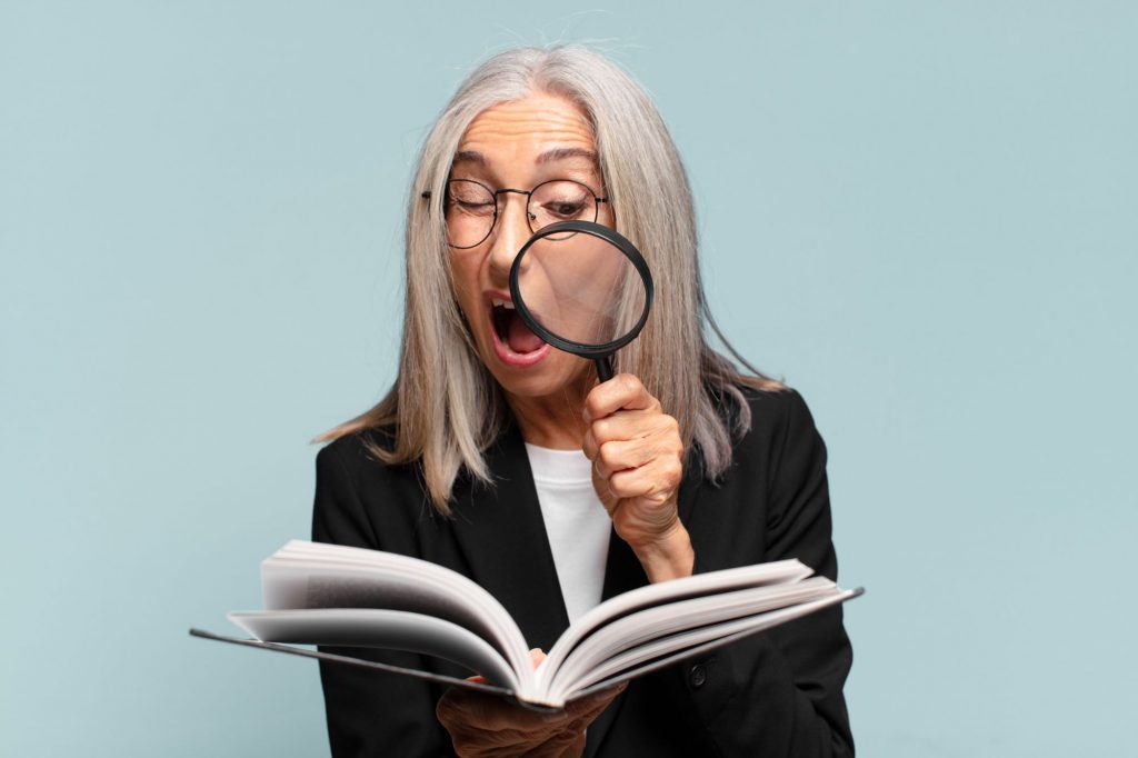 Woman-using-magnifying-glass-to-read-pages-in-book