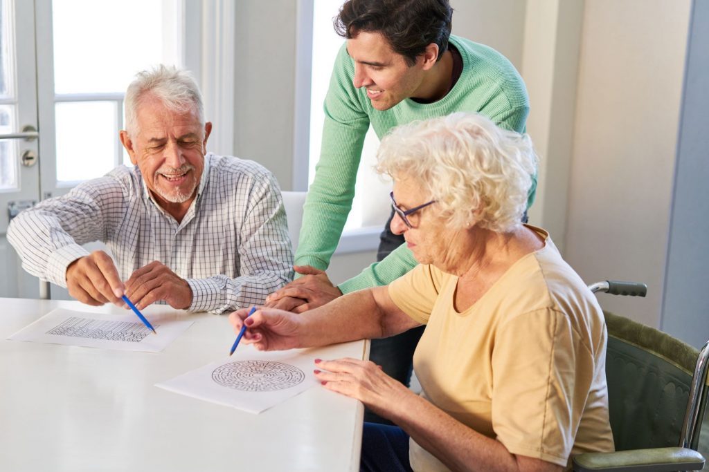 A caregiver assisting a senior man and woman with memory care activity. 