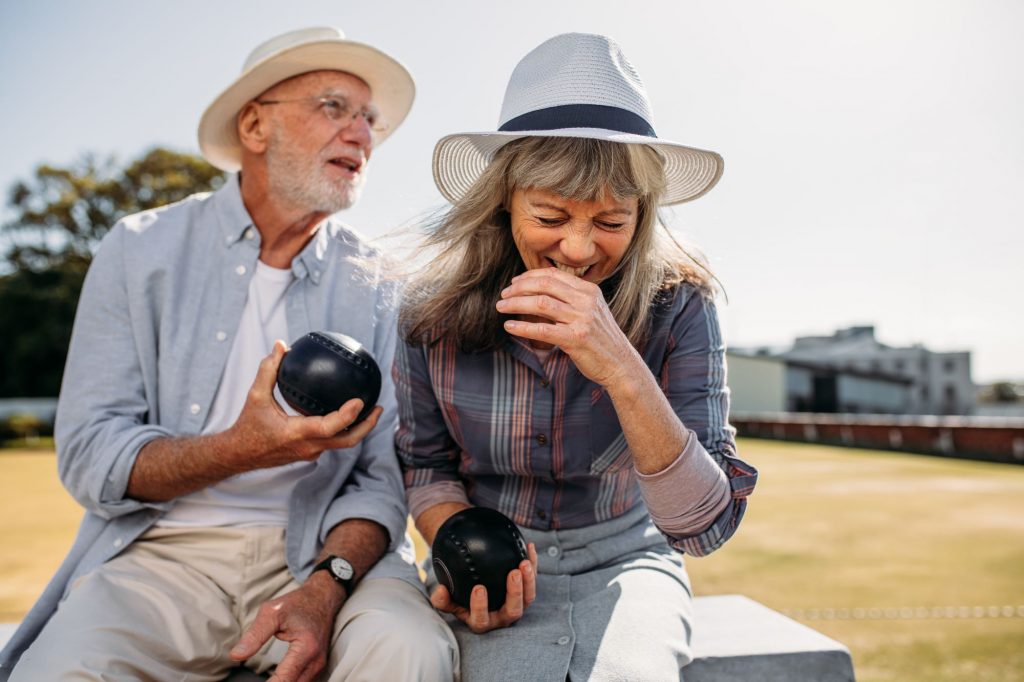 two seniors holding bocce balls and laughing in an active adult community