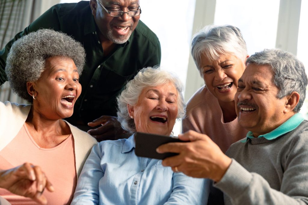 5 Ways Moving To a Retirement Community Can Improve Your Health, 5 senior citizens sitting on couch smiling and laughing with phone