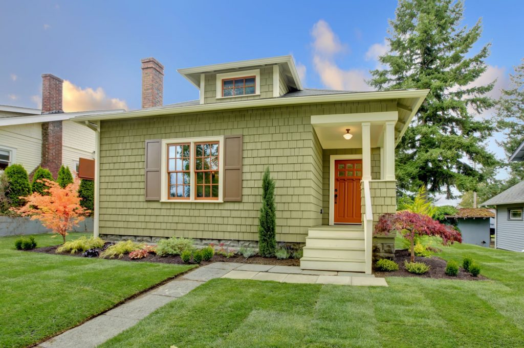 Green craftsman home with manicured lawn and stained door.