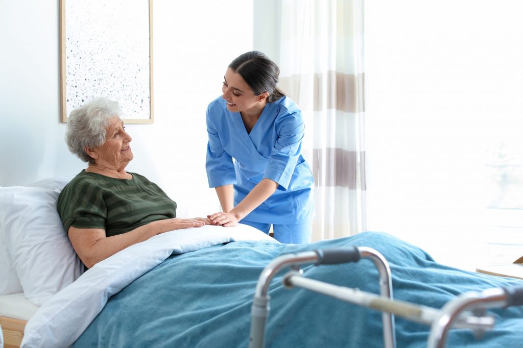 senior woman receiving hospice care in bed with a nurse by her side