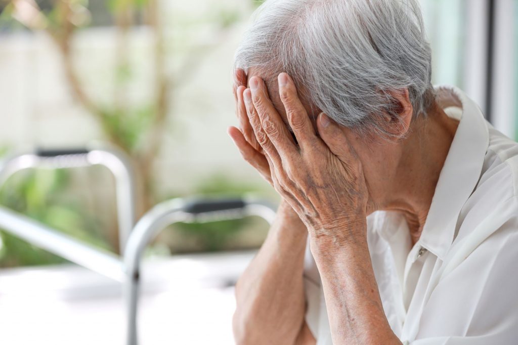 senior woman crying with hands over her face, elder abuse depiction