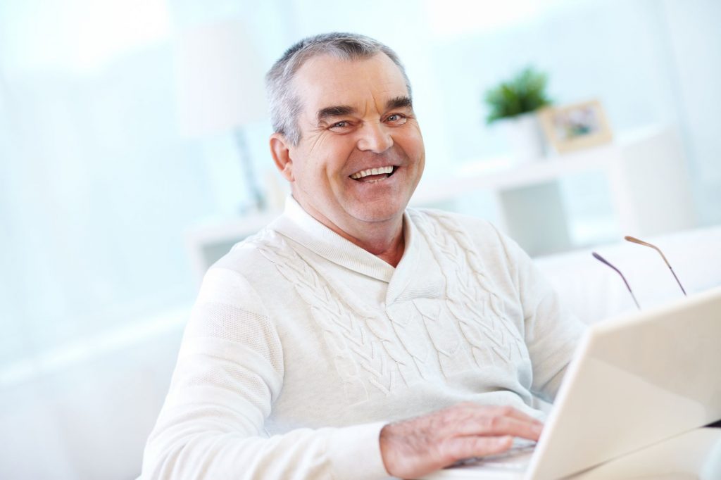 Senior male smiling in front of a computer figuring out How to Get Help as an Elder Orphan