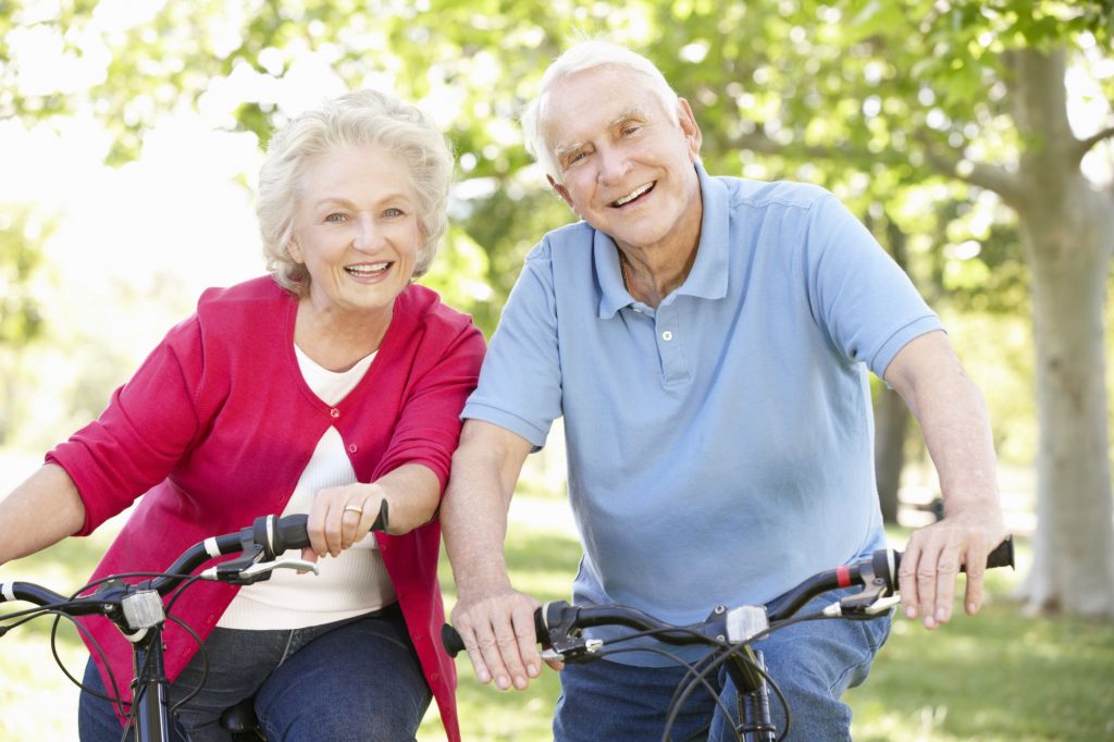 Older white couple enjoying a bike ride on a sunshiny day.