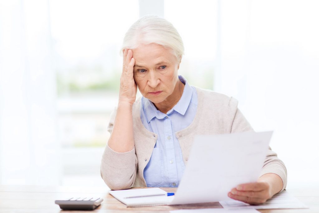 retired woman sitting at the table, reading a paper and looking confused about her annuity