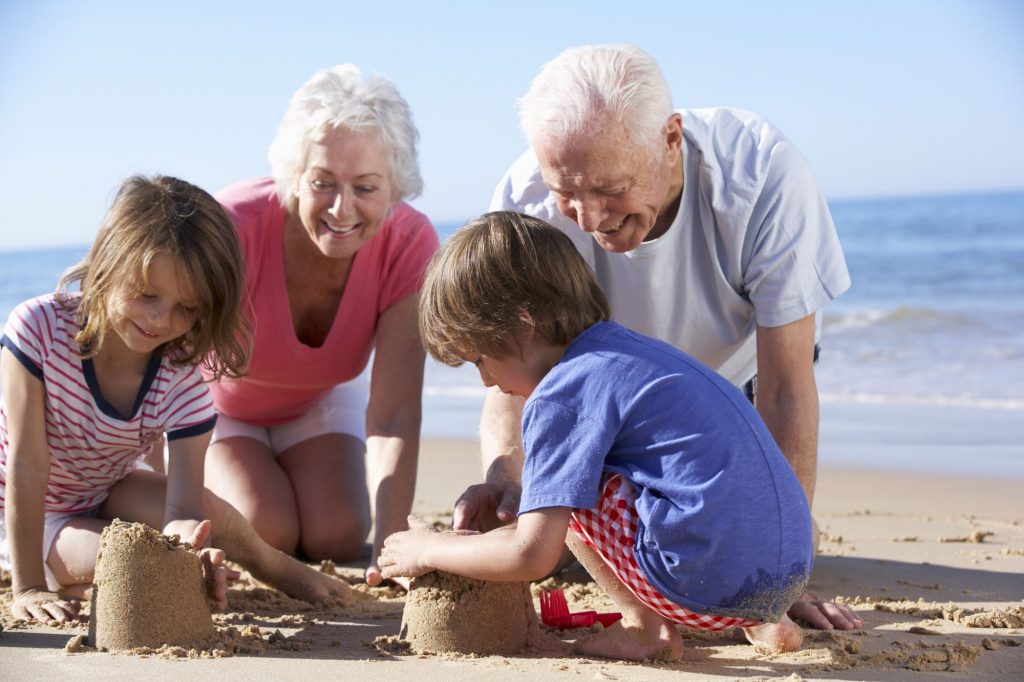 grandkids on the beach with boomer grandparents building a sand castle