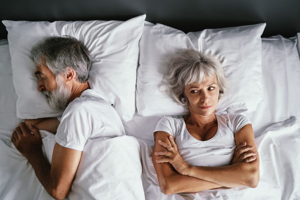 married Boomer couple in bed, woman annoyed that her husband is snoring, probably from sleep apnea