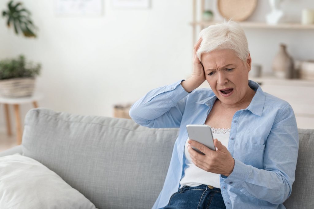 shocked grandma looking at phone, likely being scammed