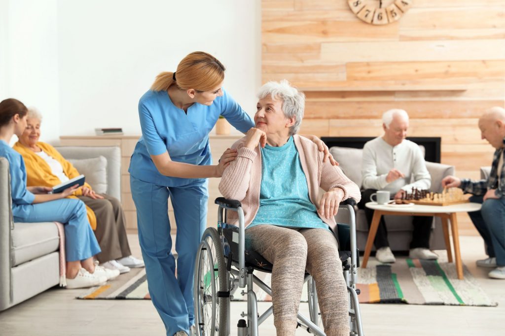 A redheaded nurse assisting an elderly woman in a well-lit nursing home.