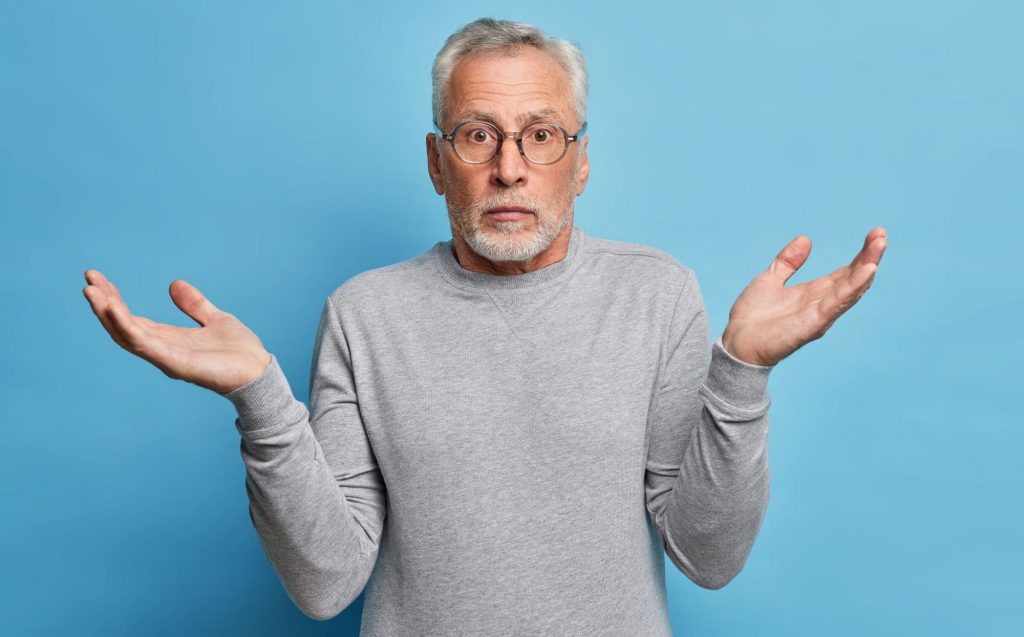 55+ man shrugging in front of a plain blue background