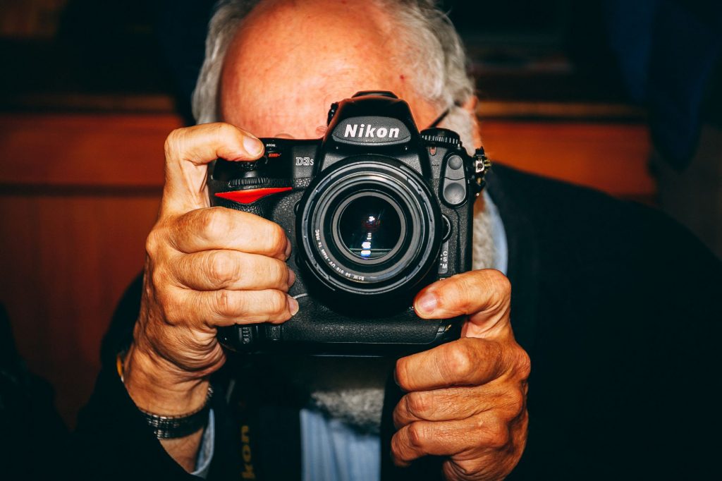 Elderly gentleman brandishing heavy-duty Nikon camera.