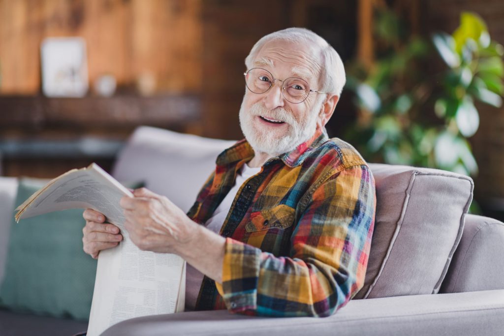 senior man sitting on the couch smiling with a newspaper in his hands