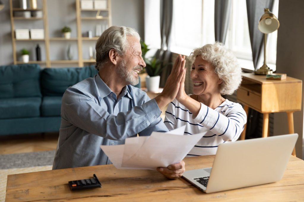 retired couple high fiving over computer and papers