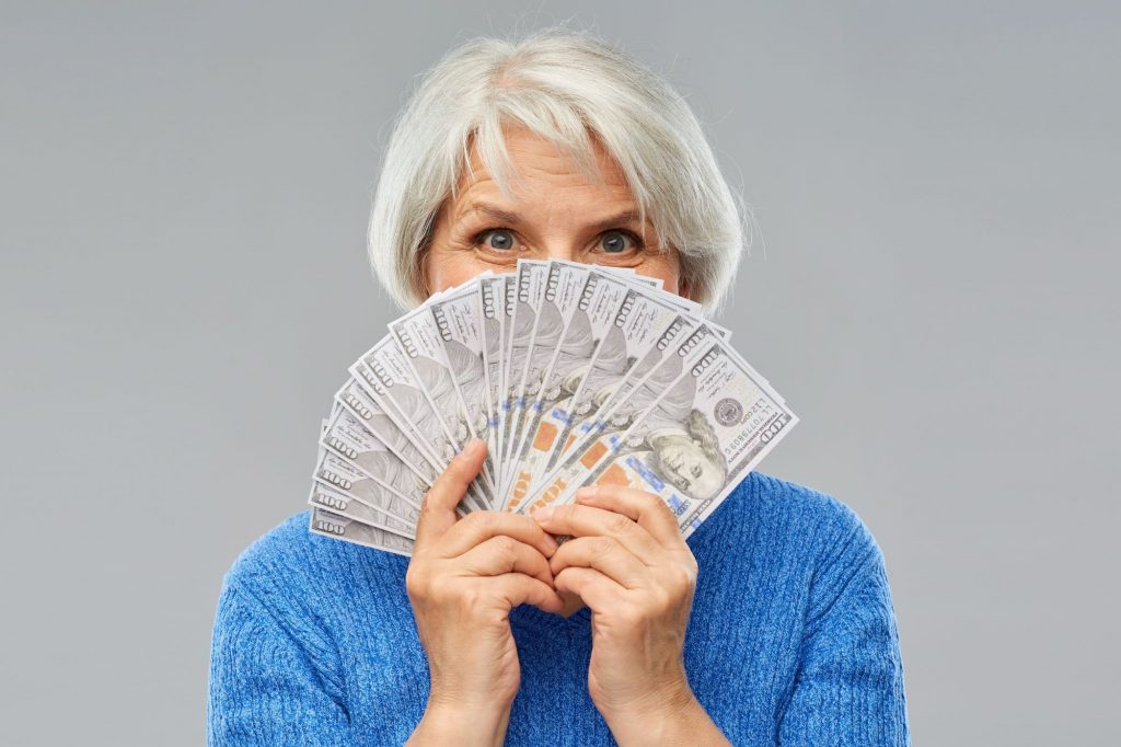 woman retiree with fan of money in front of face