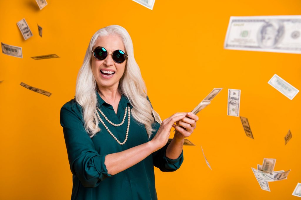 senior woman smiling with dollar bills floating around her - make extra money