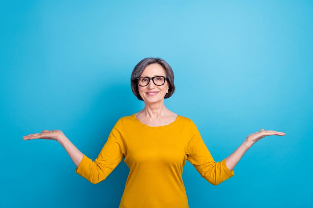 Boomer lady in yellow shirt with arms splayed against blue background.