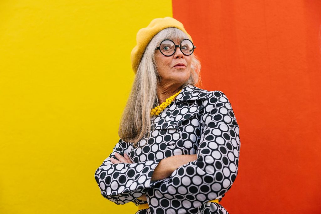 Boomer lady in yellow beret and black-and-white coat standing against a colorblock background. - tips for boomers