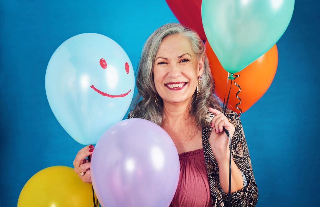 senior adult woman smiling with lots of balloons on her birthday