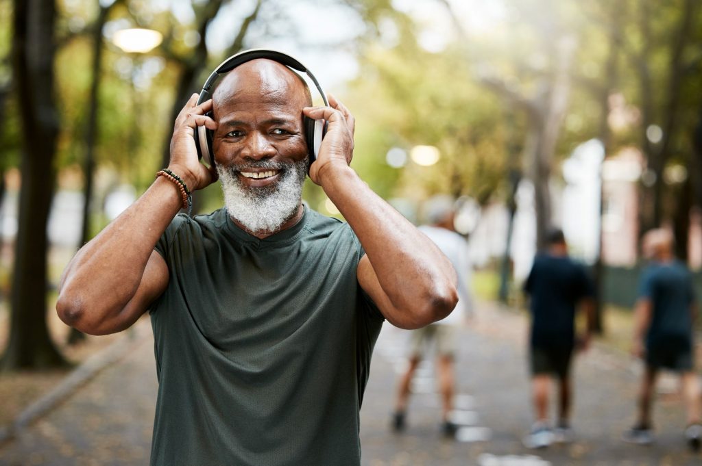 African American Baby Boomer walking in the park listening to podcast on headphones