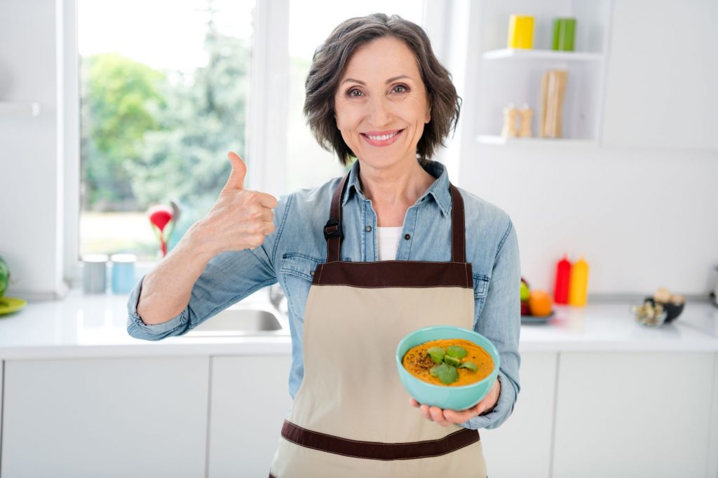 senior woman holding bowl of soup and giving thumbs up