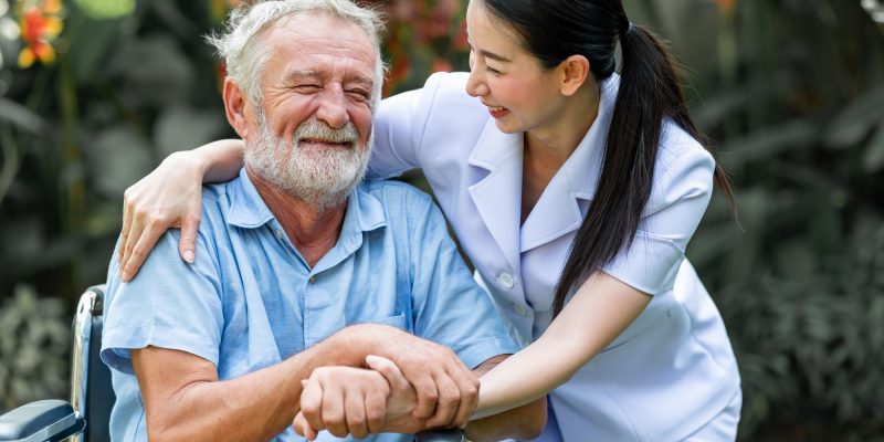 senior man in wheelchair with oriental female nurse by his side