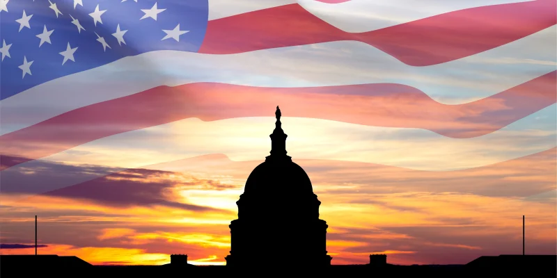 United States Capitol building silhouette and US flag against the sunset