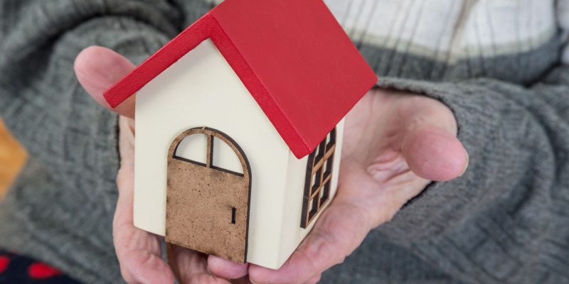 senior hands holding toy house to represent reverse mortgage