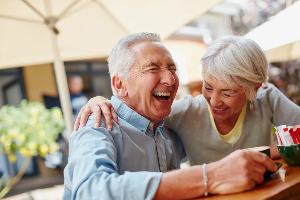 senior couple eating outside on the patio at their retirement community laughing and having fun together