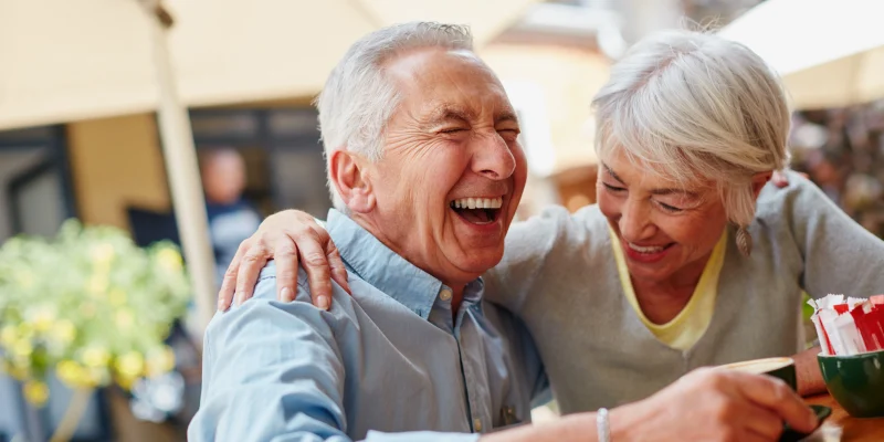 senior couple eating outside on the patio at their retirement community laughing and having fun together