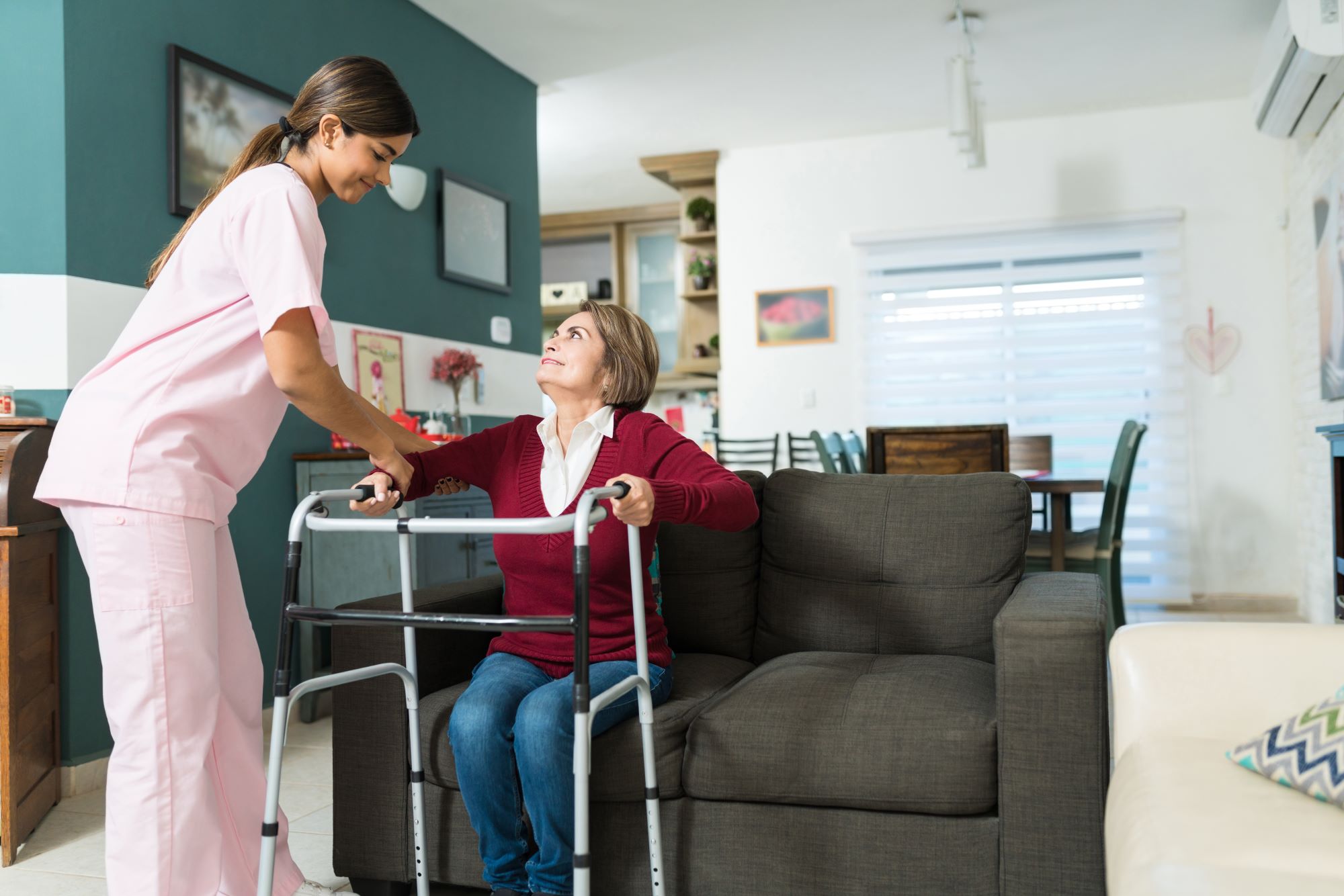 Aide helping woman in long-term care facility stand up with walker
