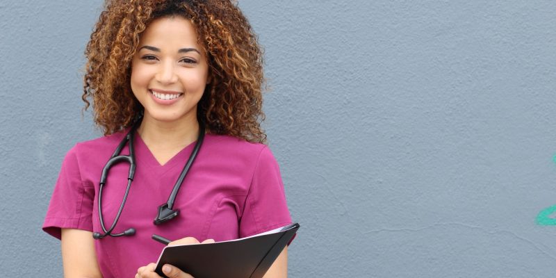 nurse with curly hair smiling and holding clipboard