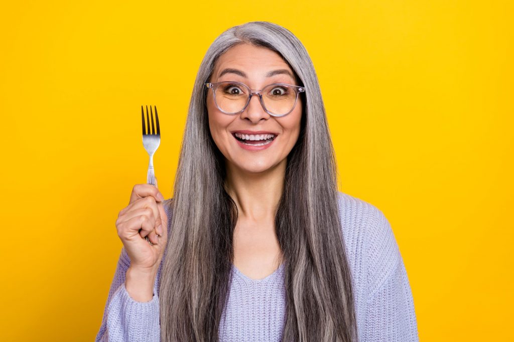 senior woman holding up fork with yellow background