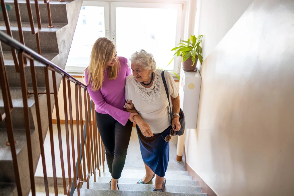 young adult woman helping senior woman up steps in a home