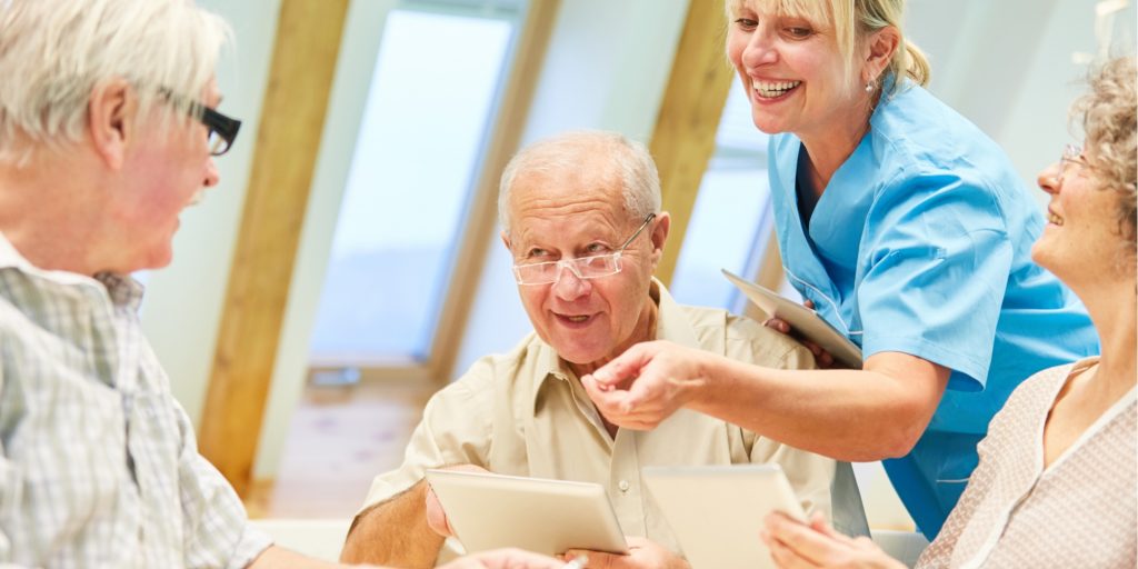 smiling seniors at a table talking to a nurse in an assisted living facility