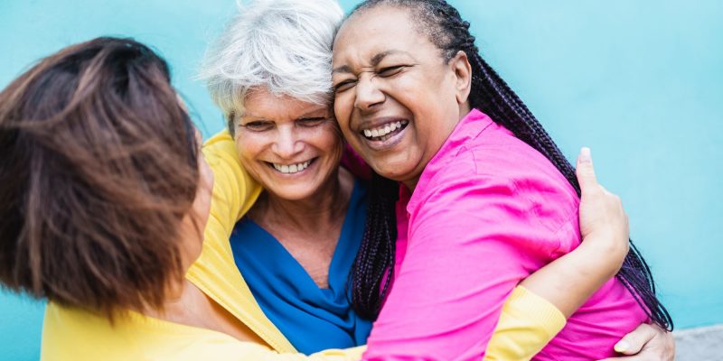 three senior friends hugging and smiling