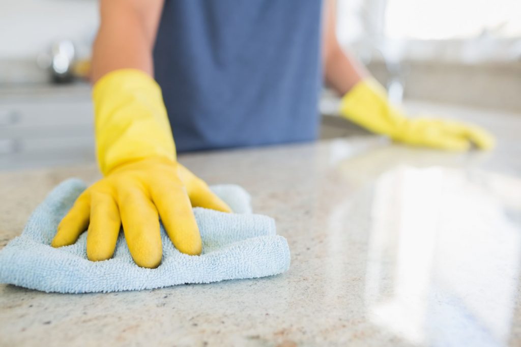 Person with yellow rubber gloves wiping down a counter with cloth.