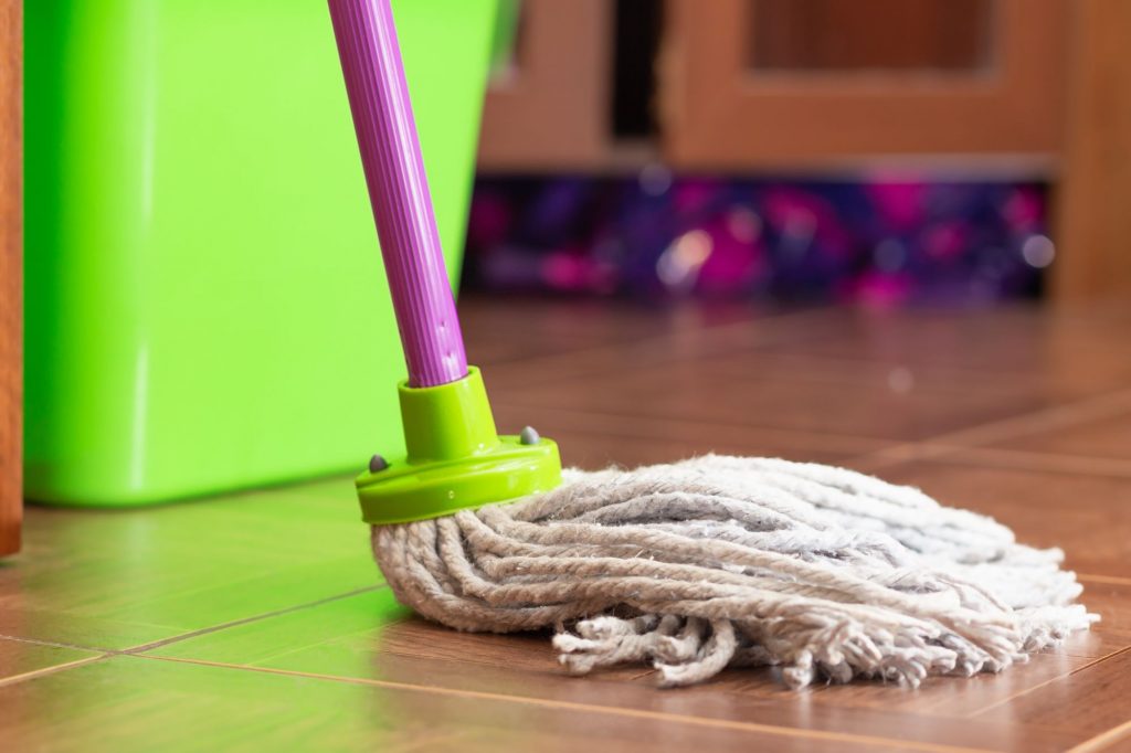 Mop with purple handle cleaning wood floor.