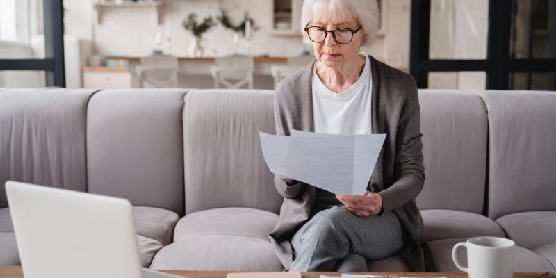 senior woman sitting on couch looking stressed with bills