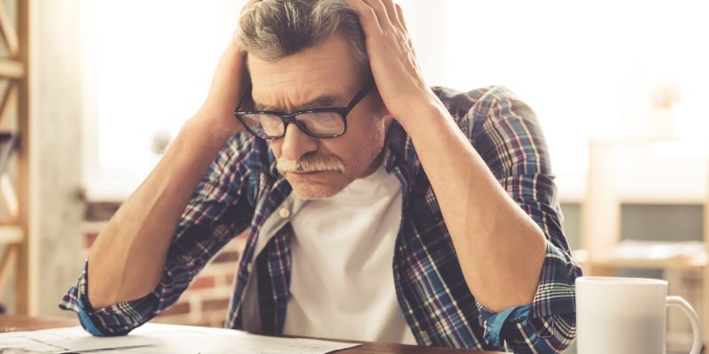 senior older adult man sitting at a desk holding his head maybe with a head ache