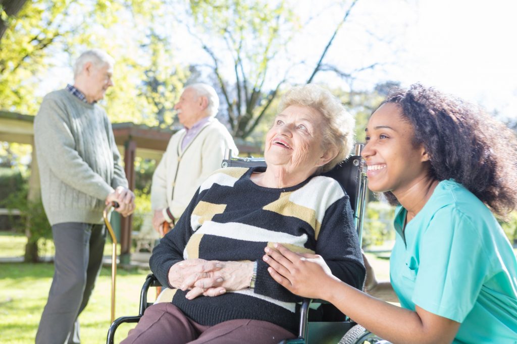 Smiling nurse outside with senior lady in a wheelchair.