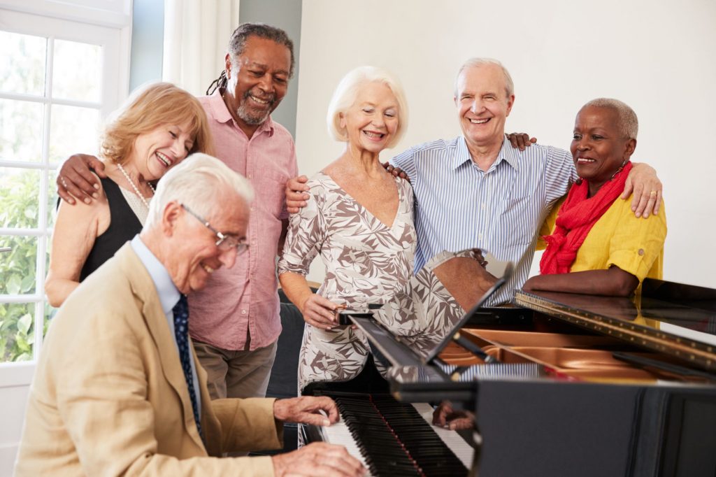 Happy seniors gathered around elderly pianist and his grand piano.