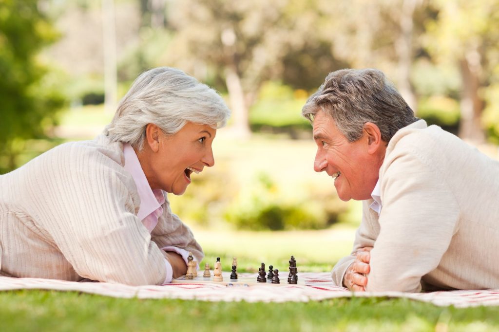 two seniors playing chess outside in a picnic like area