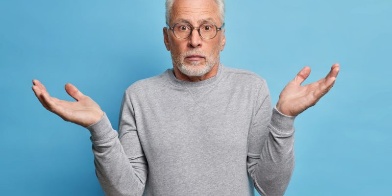 55+ man shrugging in front of a plain blue background