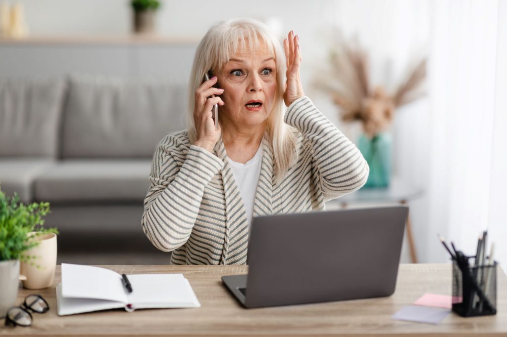 older adult saying uh oh on the phone while looking at her computer screen
