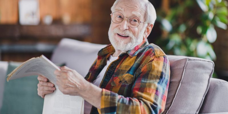 senior man sitting on the couch smiling with a newspaper in his hands