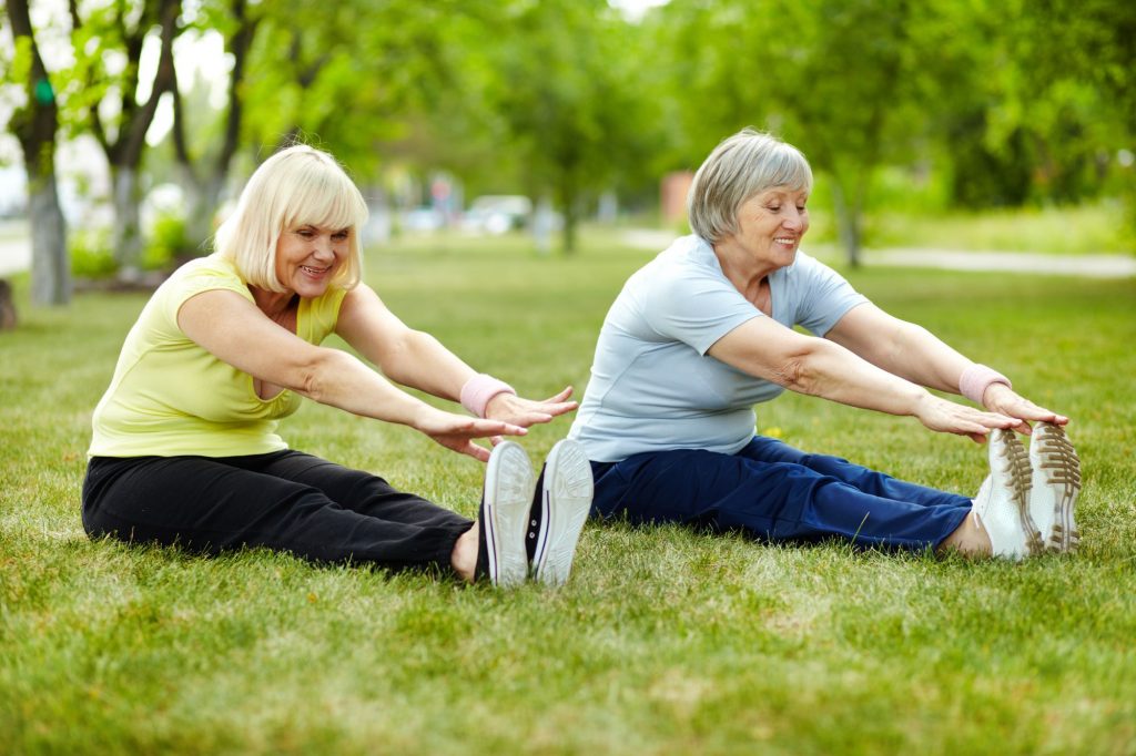 Two senior ladies in exercise clothes stretching in the park.