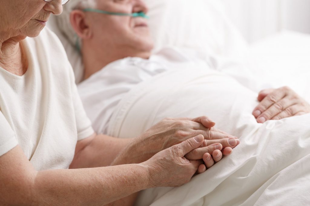 senior man in a hospital bed with wife holding hand