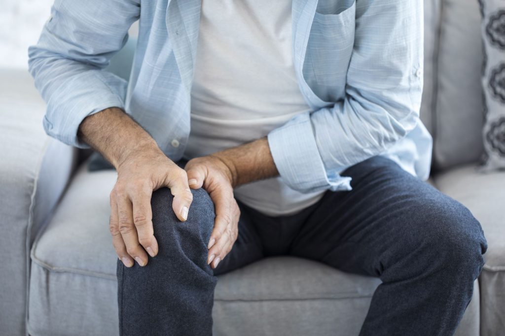 senior retiree man holding knee in pain on couch
