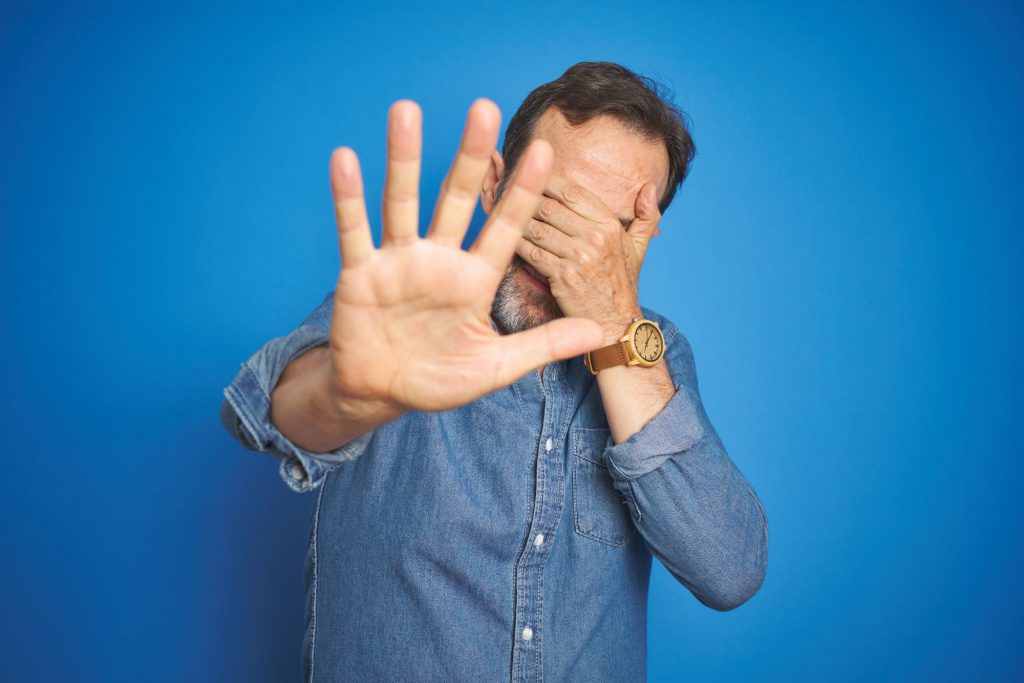 Aging man embarrassed, covering hands with face.